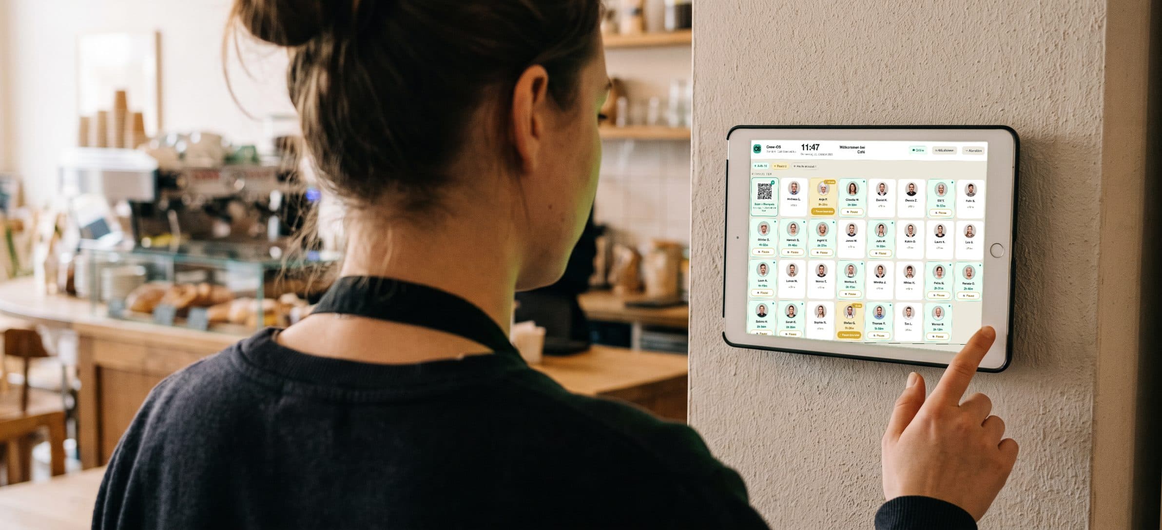 Mitarbeiterin stempelt sich im Café an der iPad-Stempeluhr von Crew-OS ein — auf dem iPad 30 Mitarbeiter mit Foto, davon 14 im Dienst mit laufender Arbeitszeit und 2 in Pause